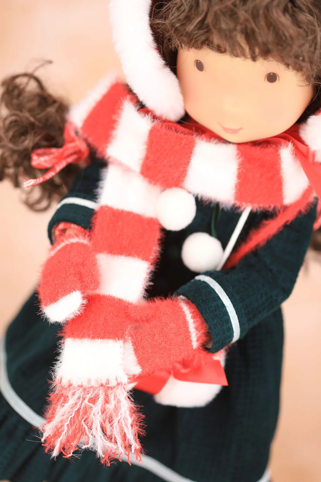 A close-up of a Holly Hobbie doll wearing a red and white striped fuzzy scarf, matching red and white striped mittens, and a dark green dress with white trim.
