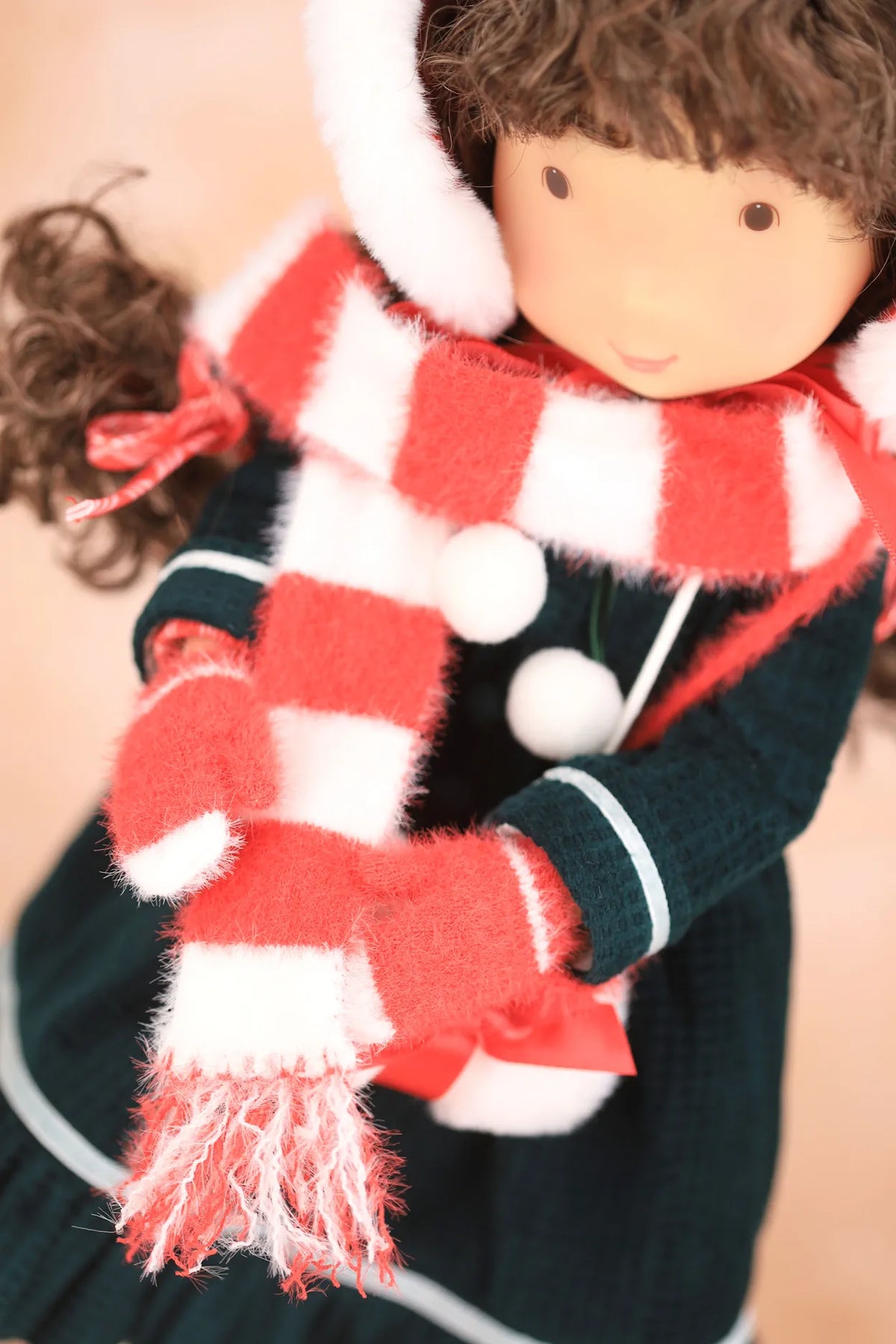 A close-up of a Holly Hobbie doll wearing a red and white striped fuzzy scarf, matching red and white striped mittens, and a dark green dress with white trim.