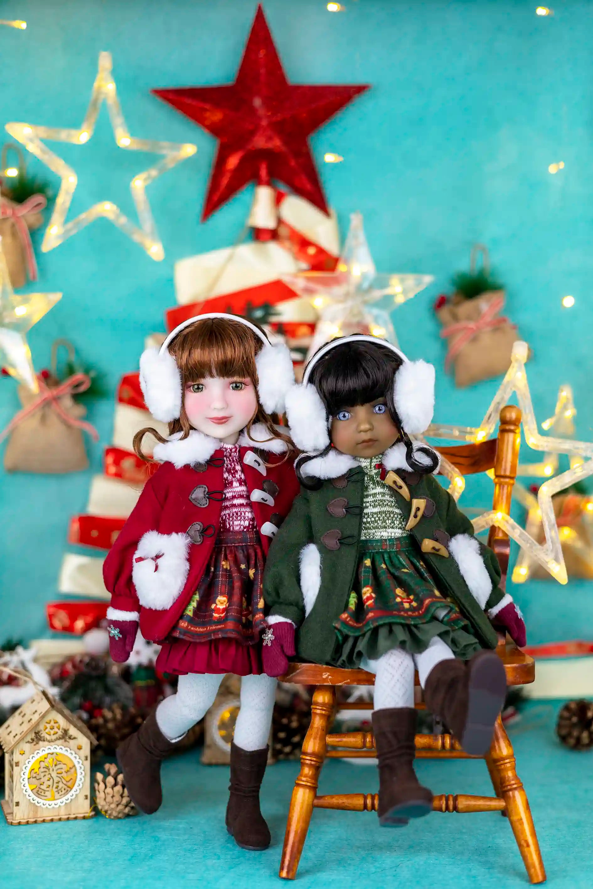 Two dolls in festive outfits sitting on a chair with a Christmas tree and decorations in the background.