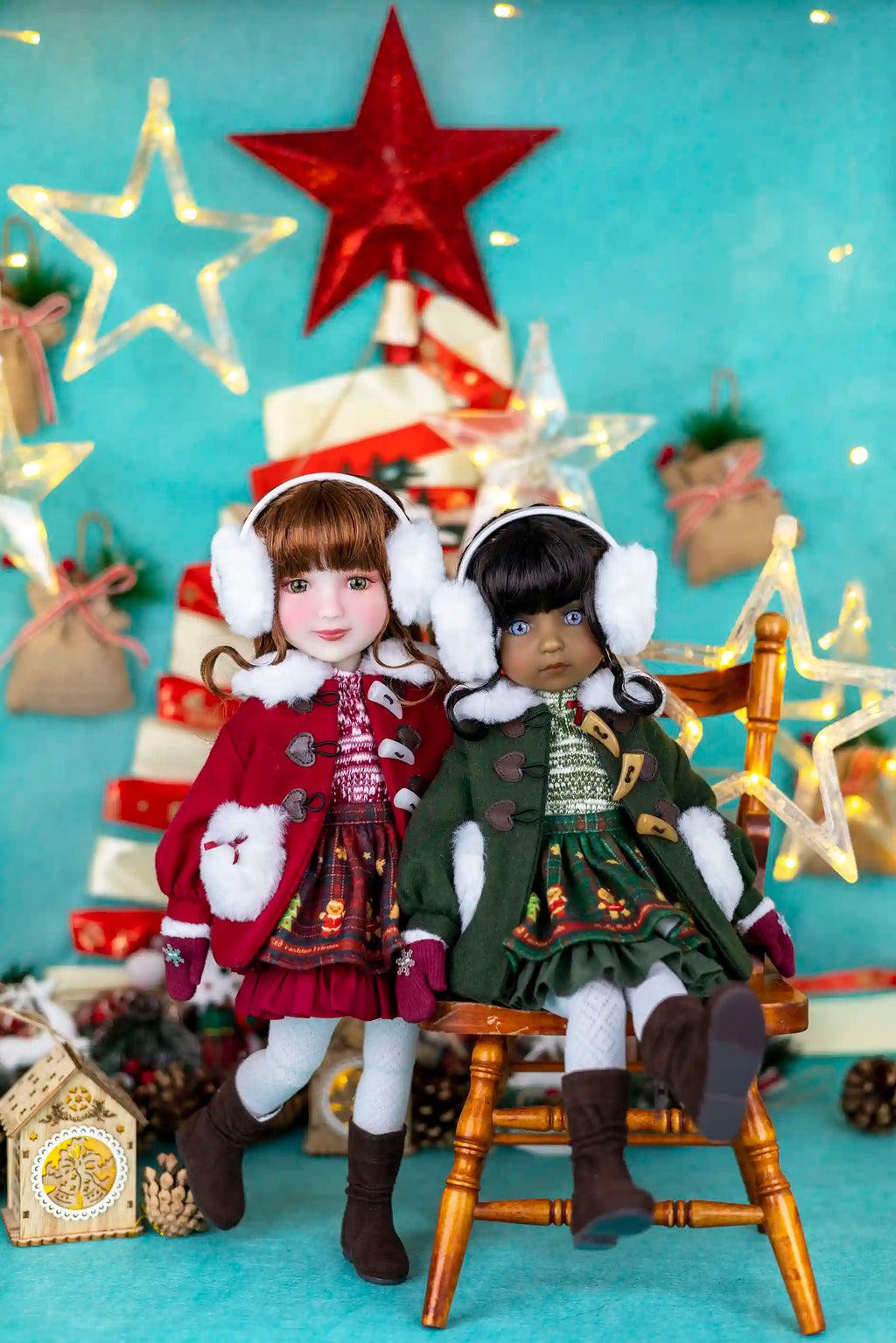 Two dolls in festive outfits sitting on a chair with a Christmas tree and decorations in the background.