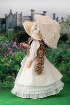Vintage-style doll with a large hat and white dress in a garden setting