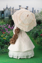 Vintage-style doll in a white dress with a lace parasol in a garden setting