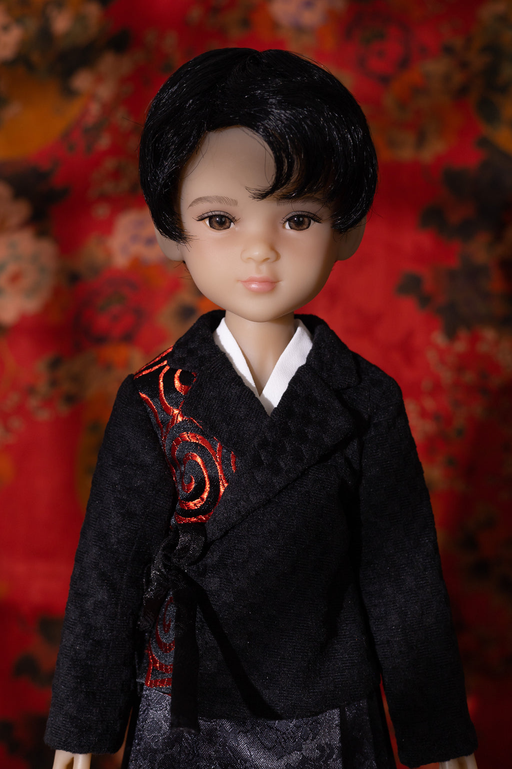 Doll wearing a traditional outfit with intricate designs against a red floral background