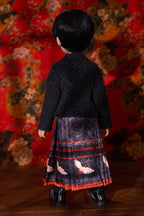 Child wearing a traditional outfit with a patterned skirt against a floral backdrop