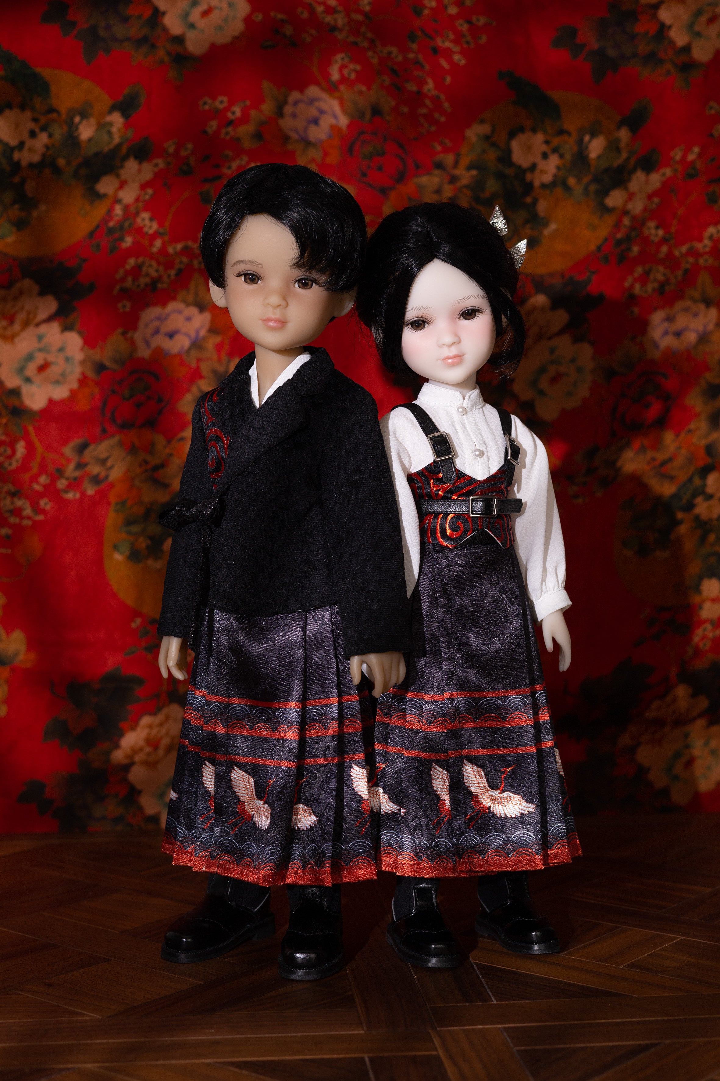 Two dolls in traditional outfits standing against a floral-patterned backdrop