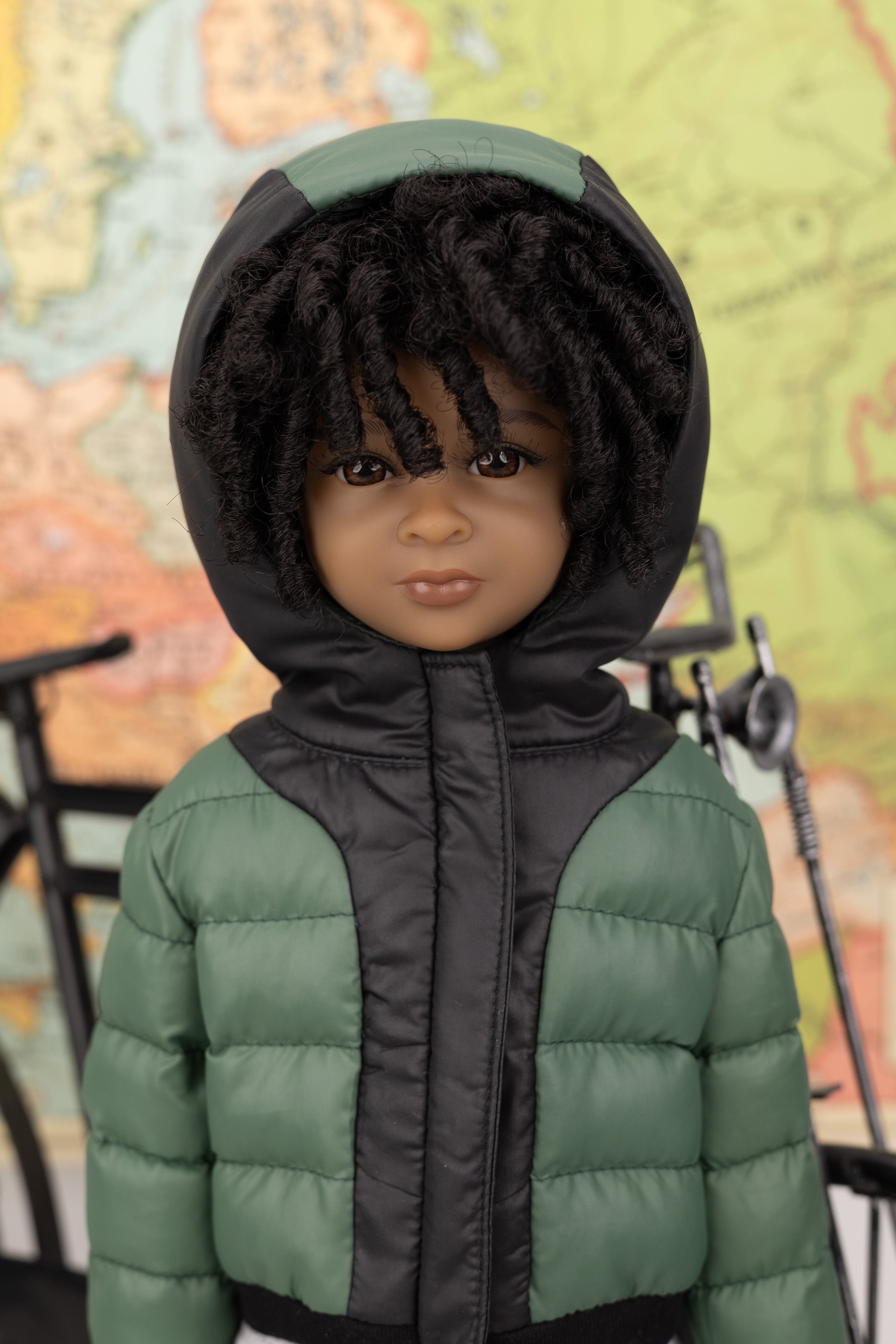 Doll wearing a green and black puffer jacket with a hood against a colorful abstract background