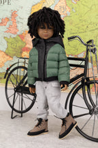 Doll wearing a green puffer jacket and gray pants, standing next to a bicycle with a world map in the background.