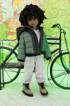 Doll wearing a green puffer jacket and gray pants standing next to a bicycle with a world map in the background