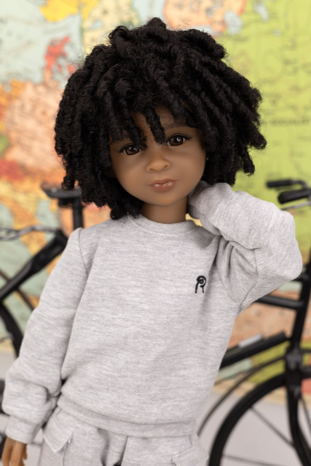 Doll with black hair wearing a gray outfit in front of a colorful background
