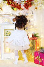 Doll in a white dress standing in a decorated room with Christmas lights and presents.