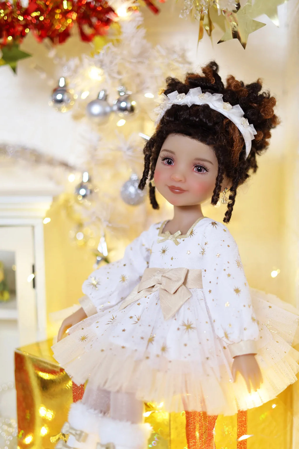 Doll in a white dress with gold stars and a bow, standing in a festive setting with lights and decorations.