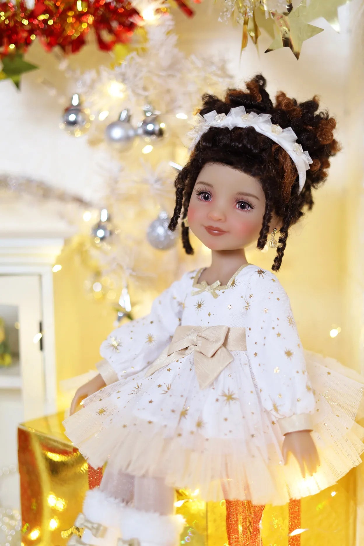 Doll in a white dress with gold stars and a bow, standing in a festive setting with lights and decorations.