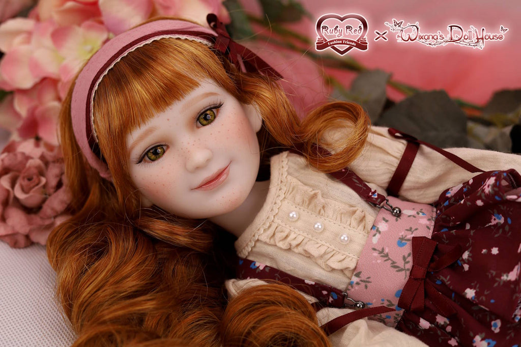 Doll with red hair and a pink headband surrounded by flowers, with branding visible.