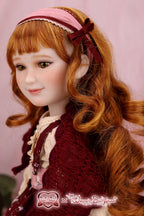 Close-up of a doll with red hair and a maroon headband against a pink background