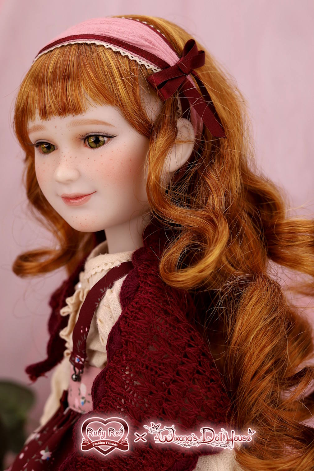 Close-up of a doll with red hair and a maroon headband against a pink background