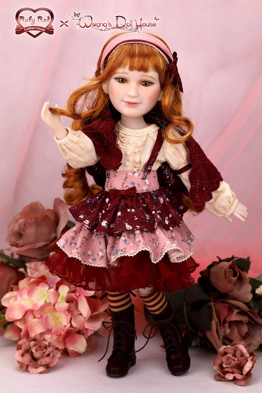 Doll with red hair and a red dress standing among flowers on a pink background