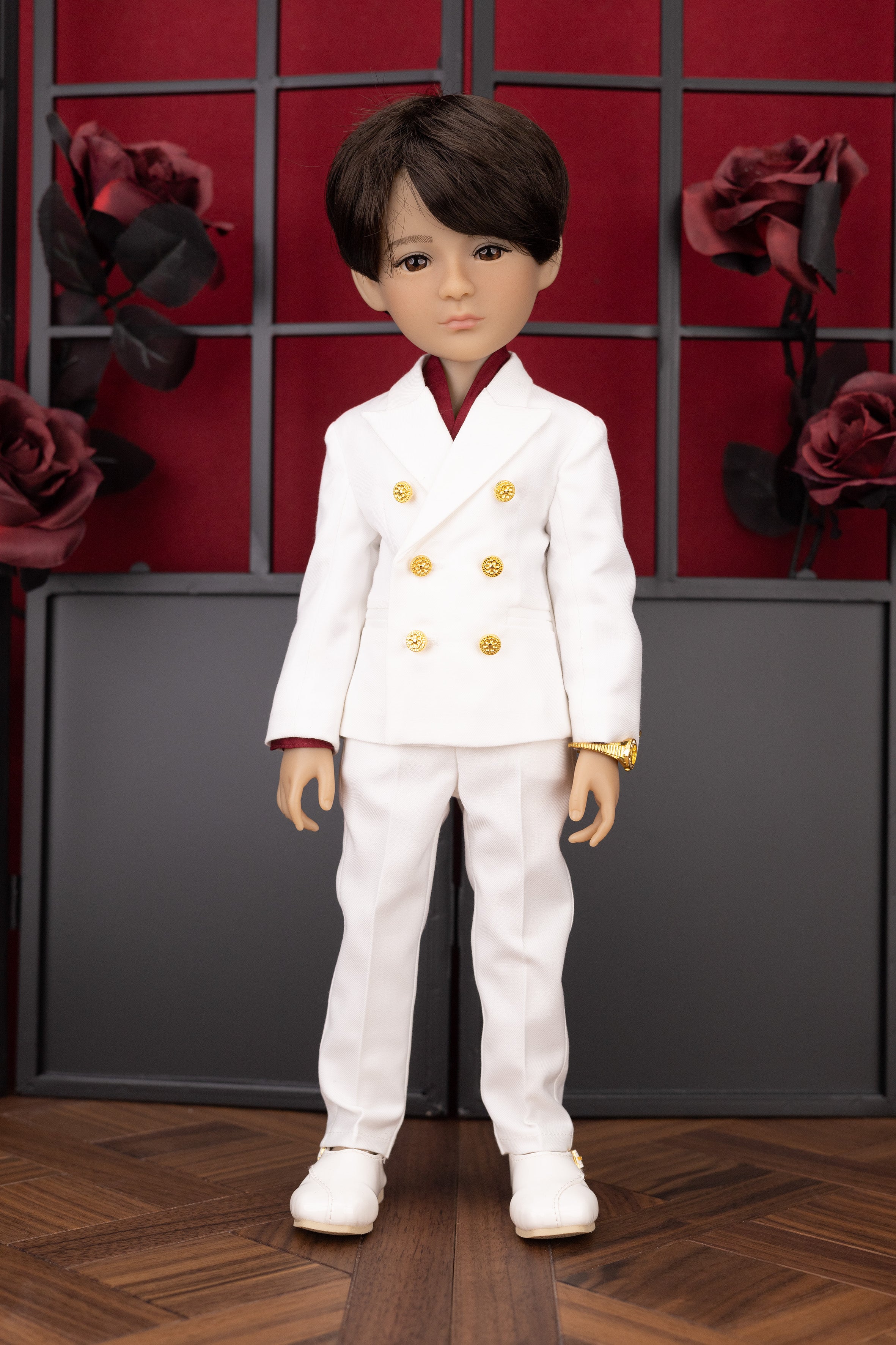 Doll in a white outfit with gold buttons against a decorative wall with red flowers.