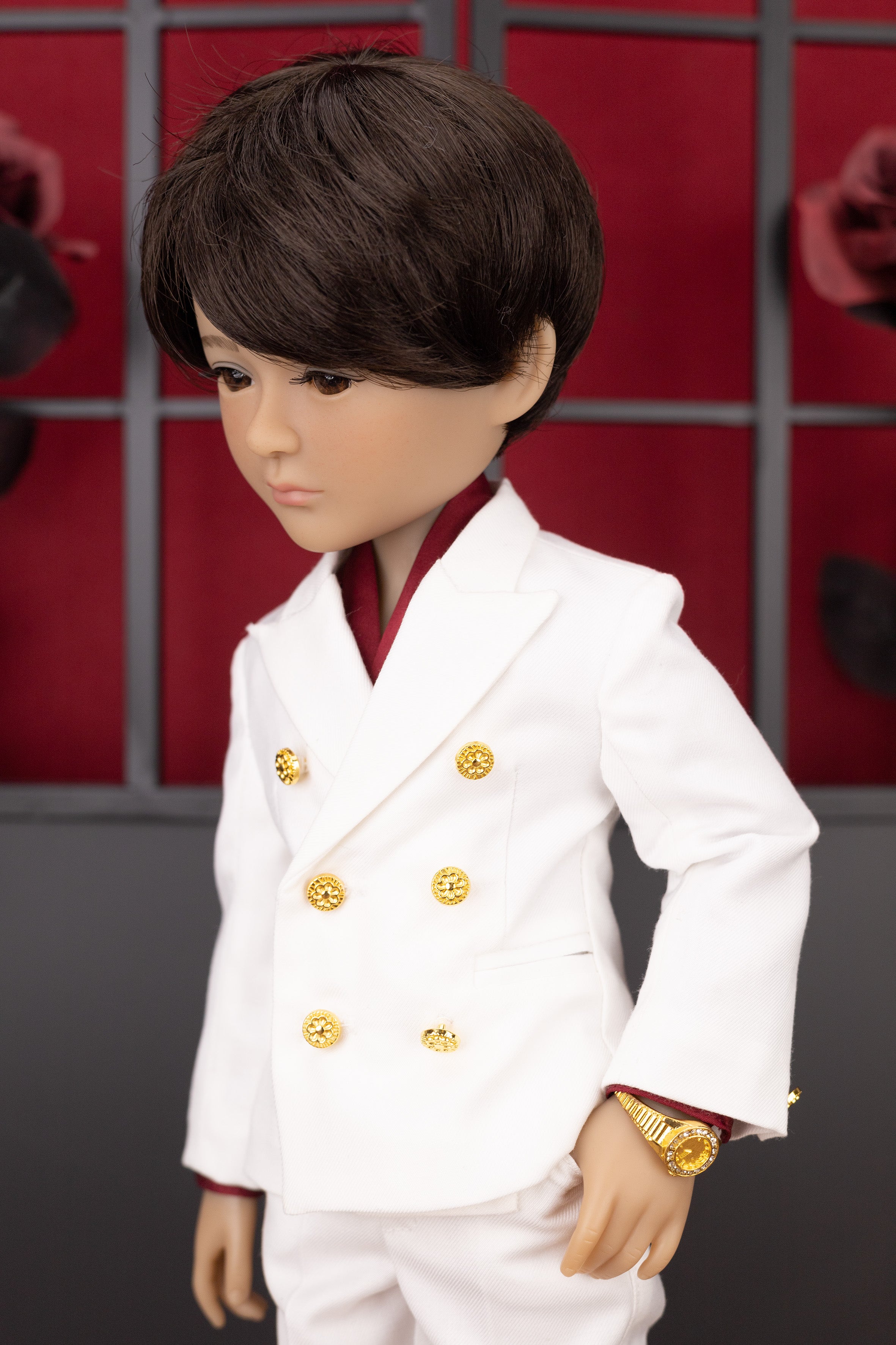 Boy doll wearing a white suit with gold buttons against a red and black checkered background