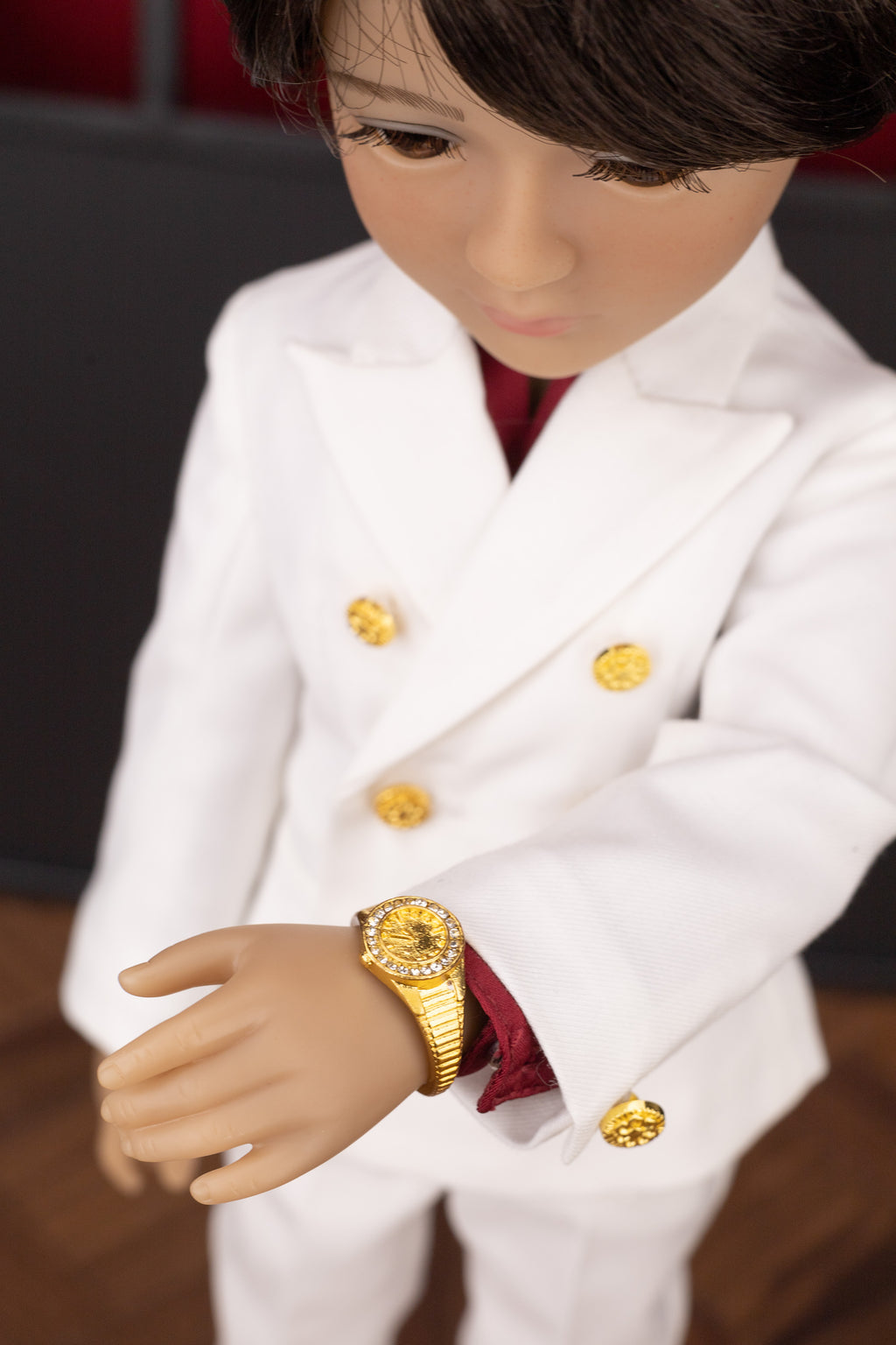 Doll wearing a white outfit with gold buttons and a gold watch, against a blurred background.