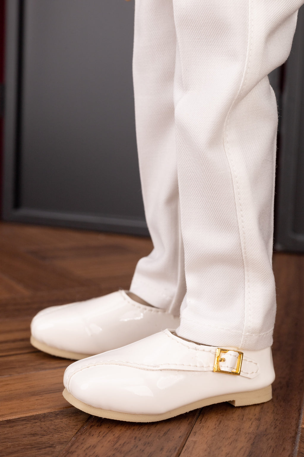 White shoes with a gold buckle worn by a person on a wooden floor.
