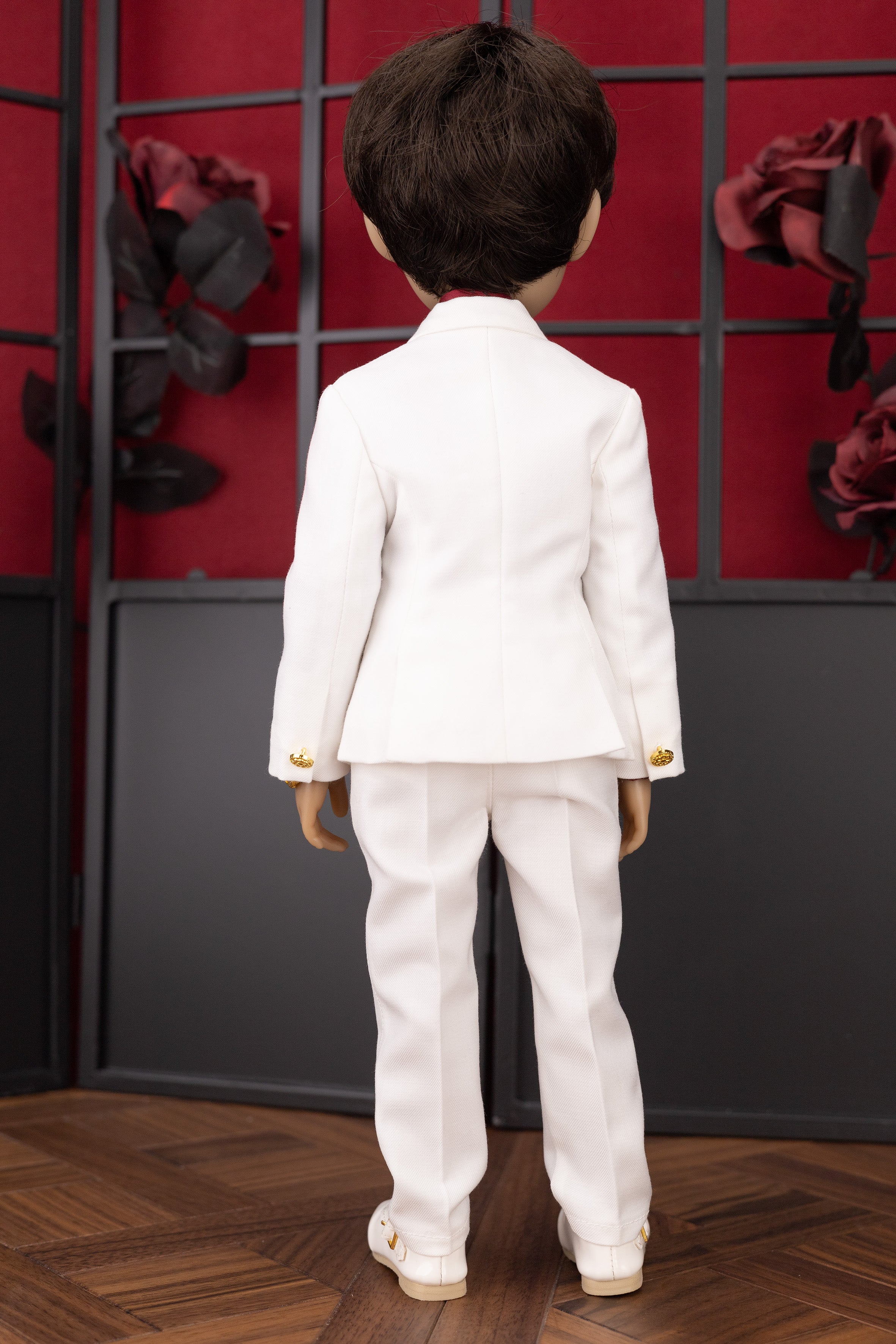 Doll wearing a white suit standing in front of a decorative wall with red and black flowers.