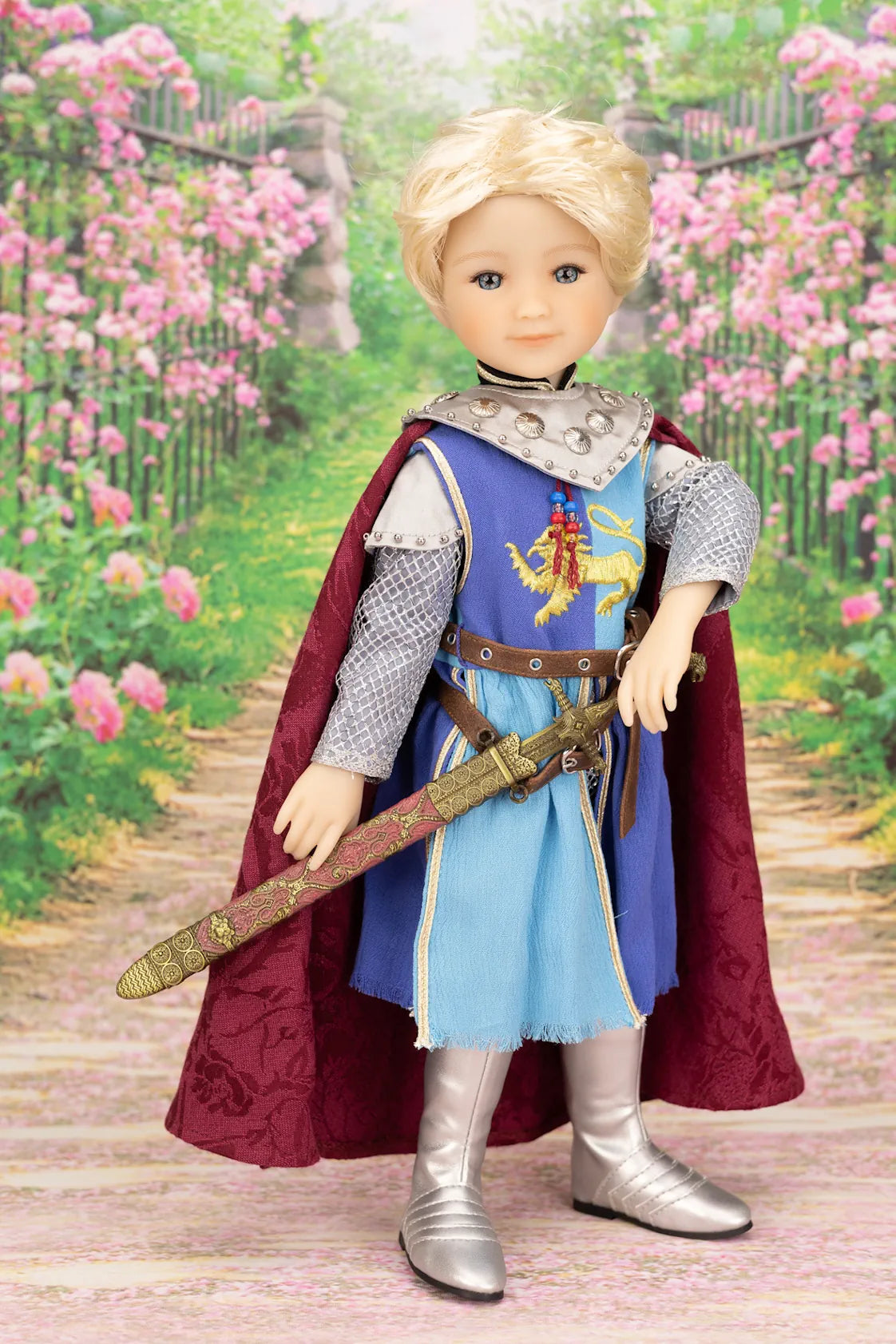 Lancelot doll in a medieval knight outfit with a sword, standing in a garden with pink flowers.