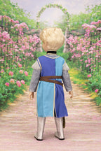 Lancelot doll in a costume standing on a path with pink flowers and an archway in the background