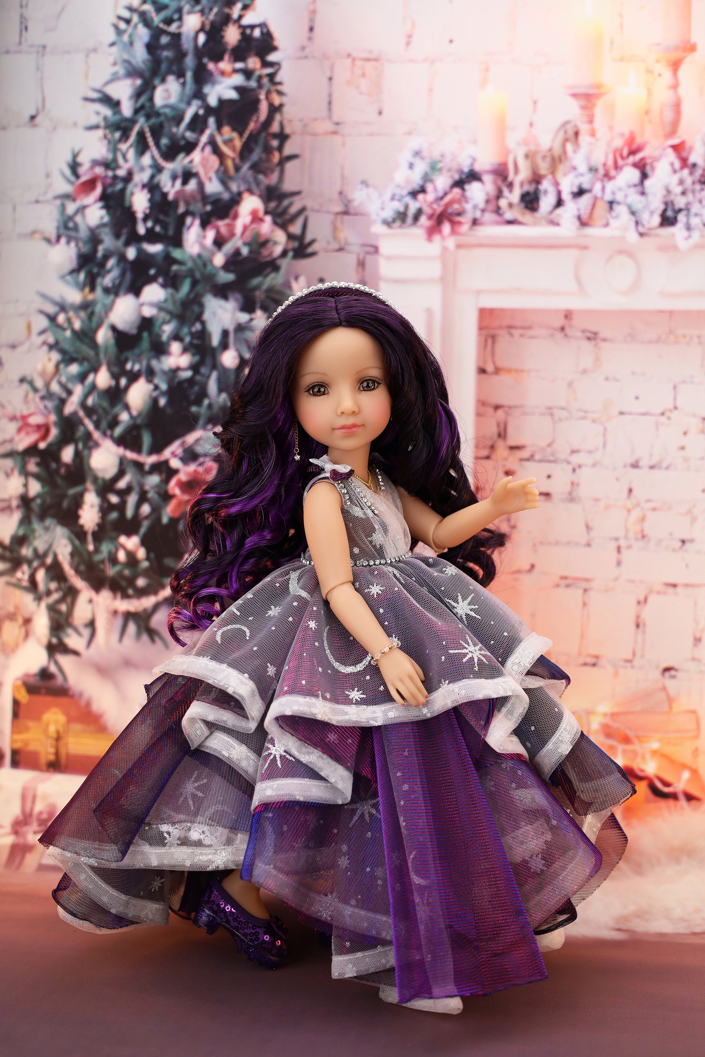 Doll in a purple dress with star patterns in a festive setting with a Christmas tree and fireplace.