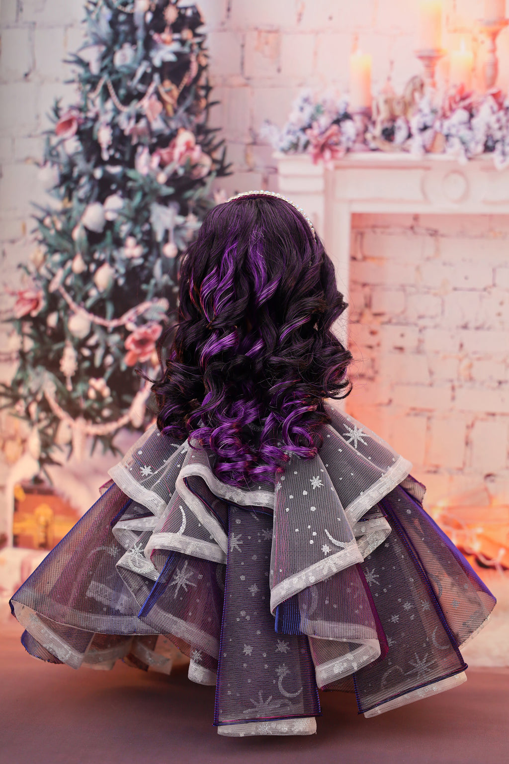 Doll in a festive setting with a decorated Christmas tree and fireplace.