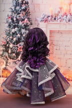 Doll in a festive setting with a decorated Christmas tree and fireplace.