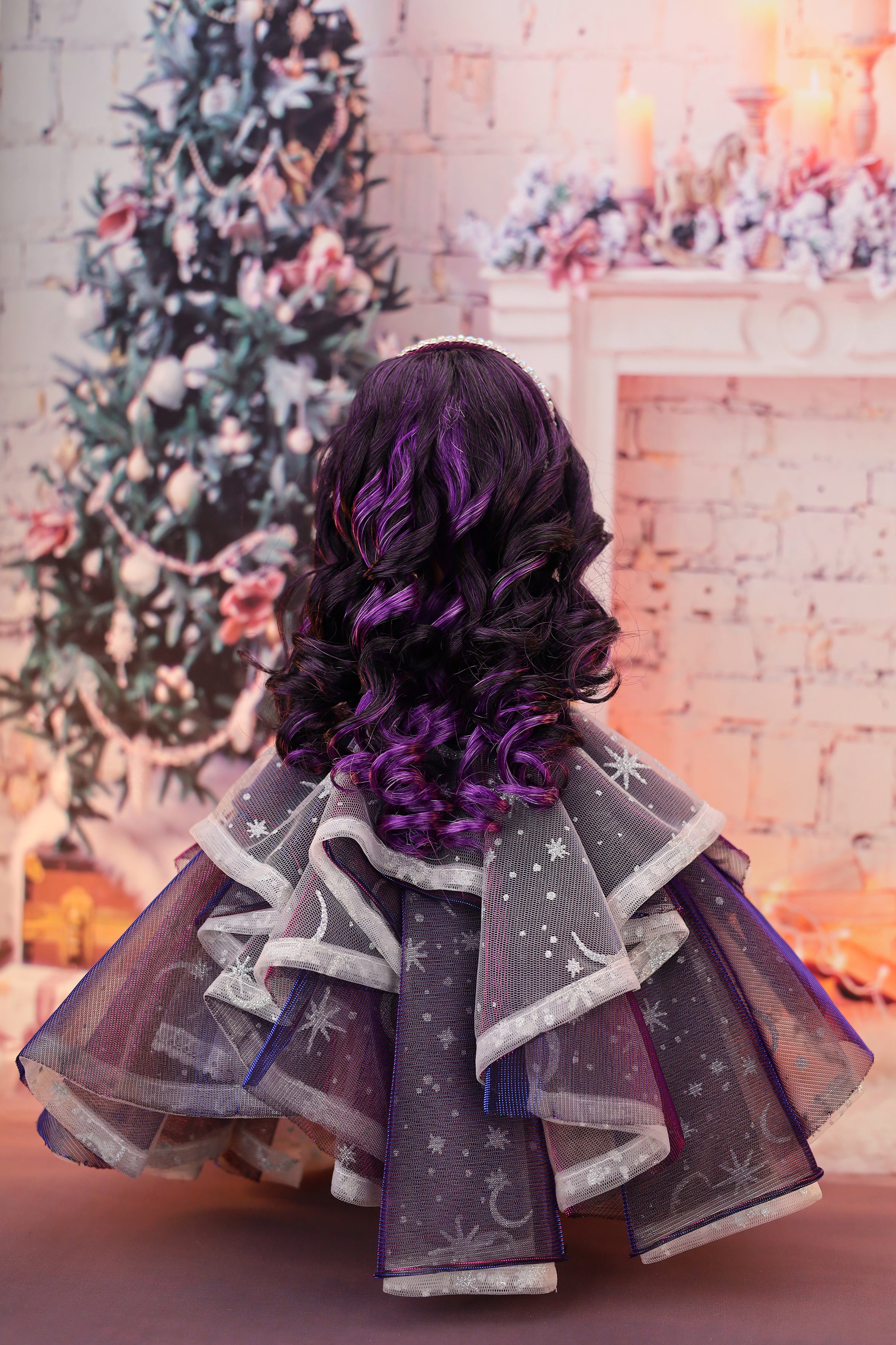 Doll in a festive setting with a decorated Christmas tree and fireplace.