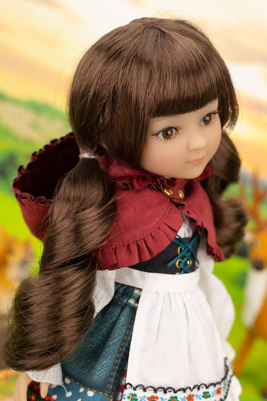 Doll with long brown hair styled in pigtails, wearing a red hooded cloak and traditional outfit.