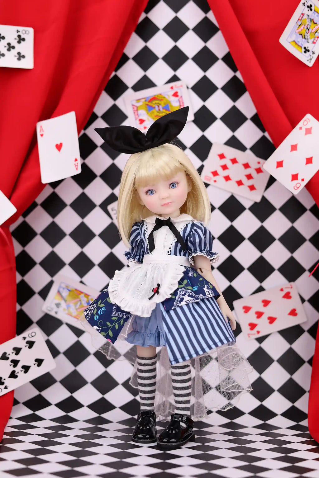 Doll in a striped dress with playing cards on a checkered floor