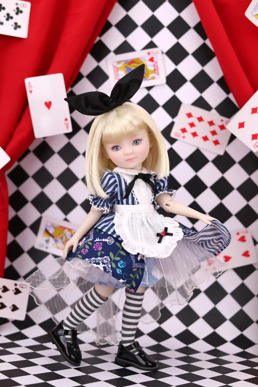 Doll in a blue dress with a black bow on a checkered floor with playing cards