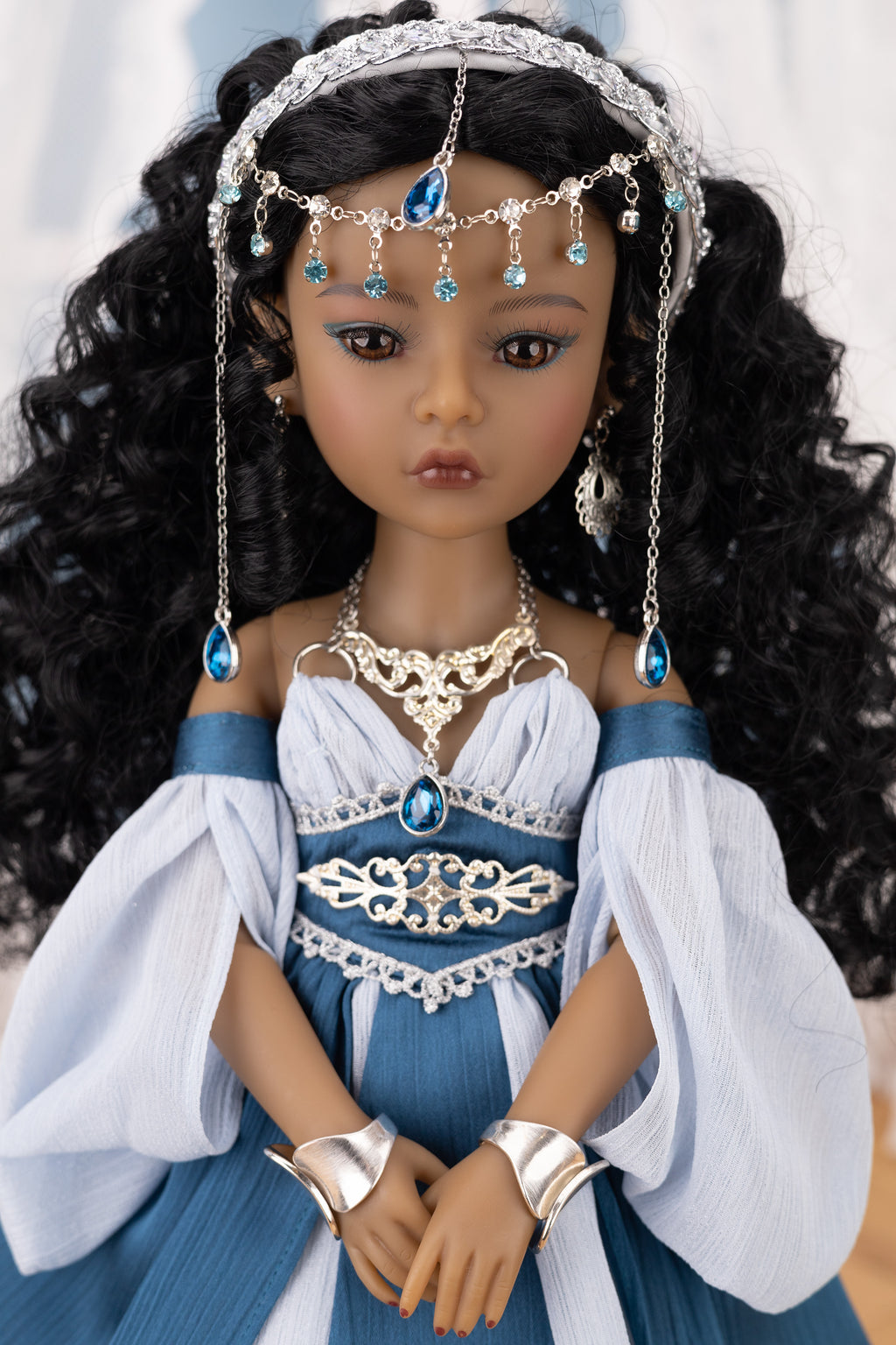 Doll in a blue and white outfit with jewelry against a neutral background