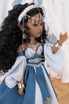 Doll in a blue and white dress with jewelry against a blurred background