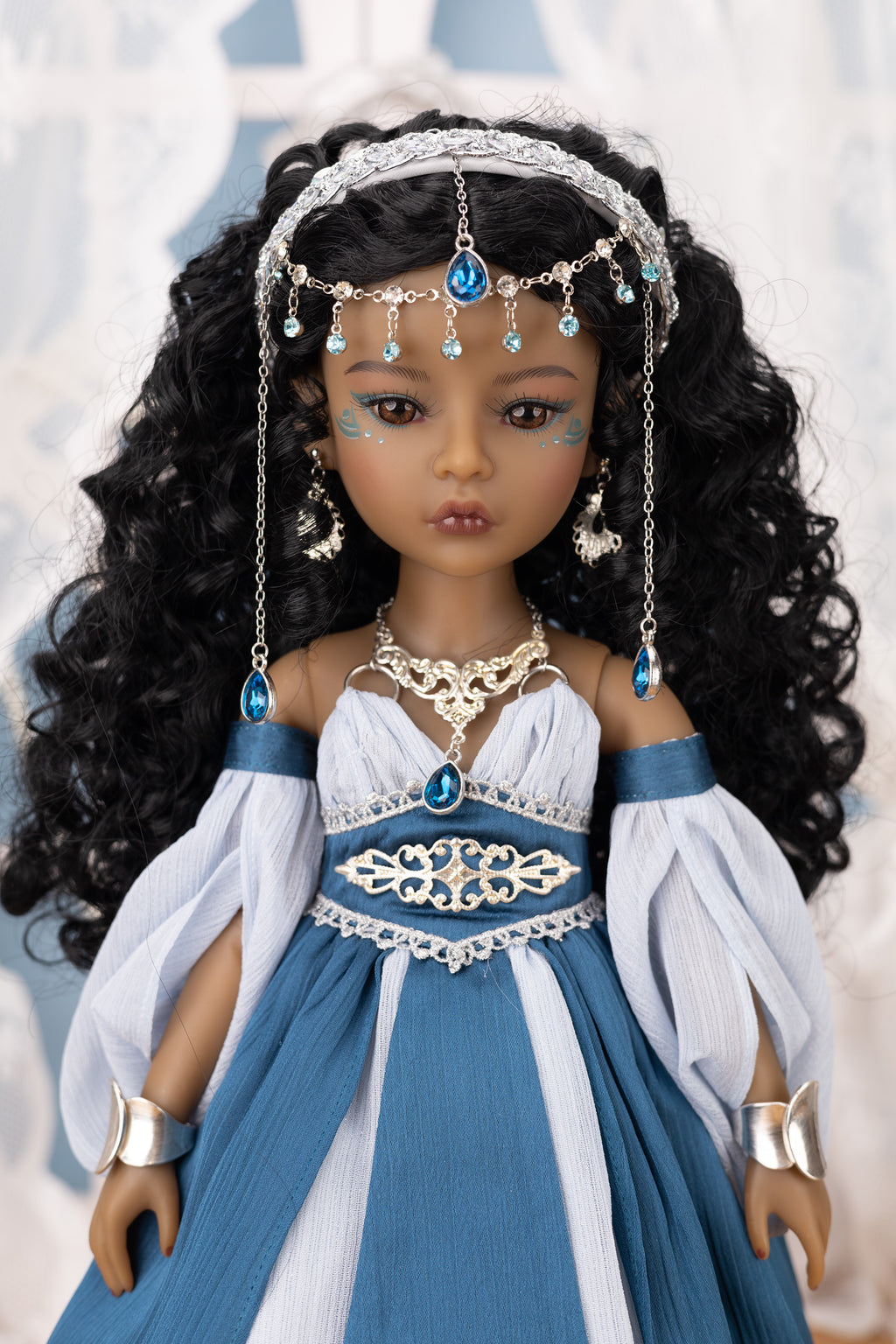 Doll in a blue and white dress with jewelry against a blurred background