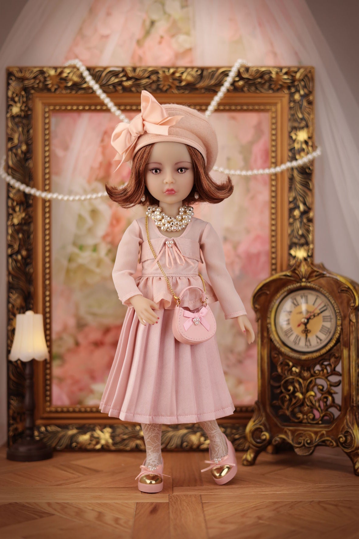 Lou in a pink dress with accessories standing in front of an ornate frame and clock.
