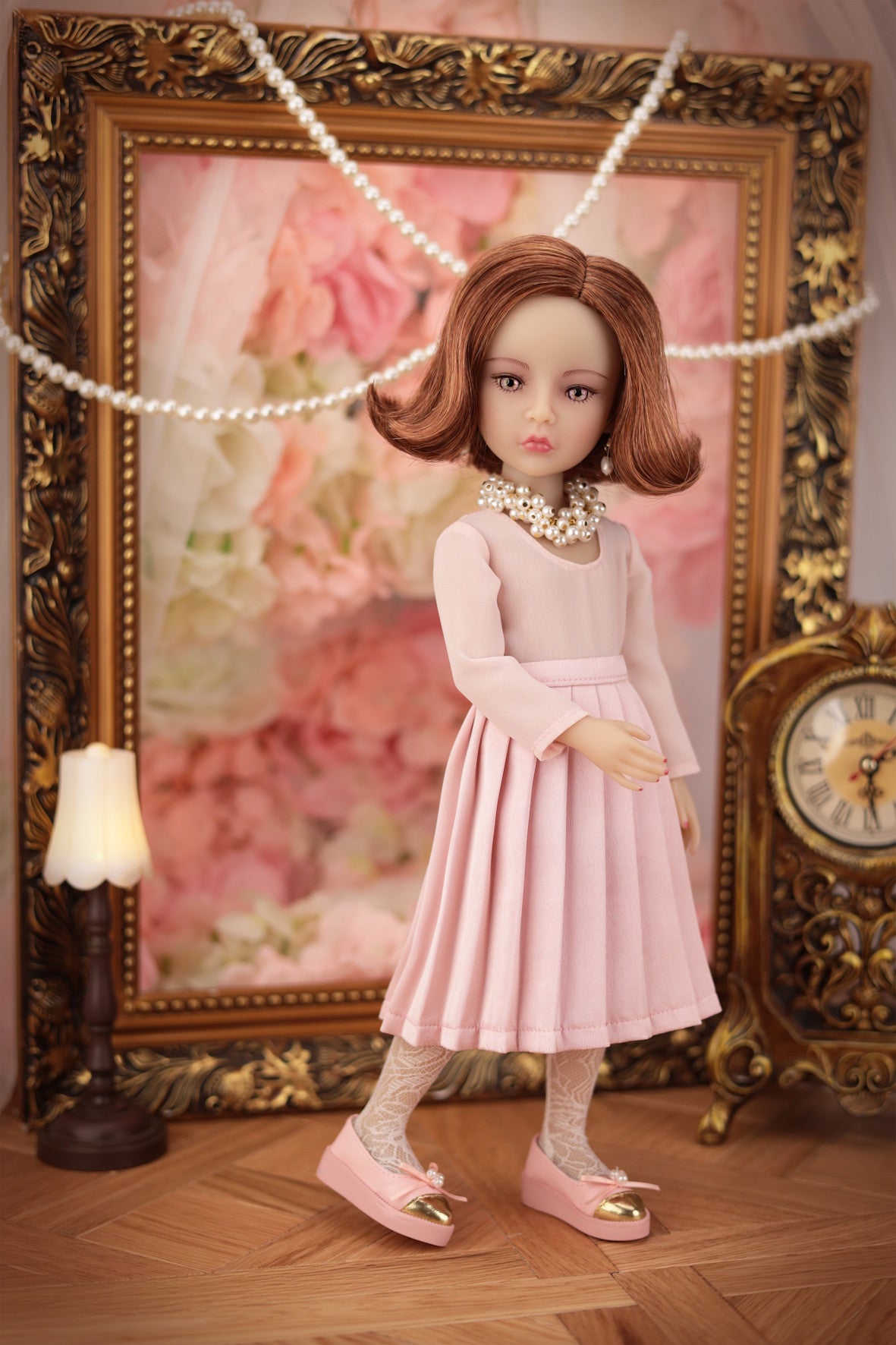 Lou in a pink dress standing in front of an ornate frame with floral artwork.