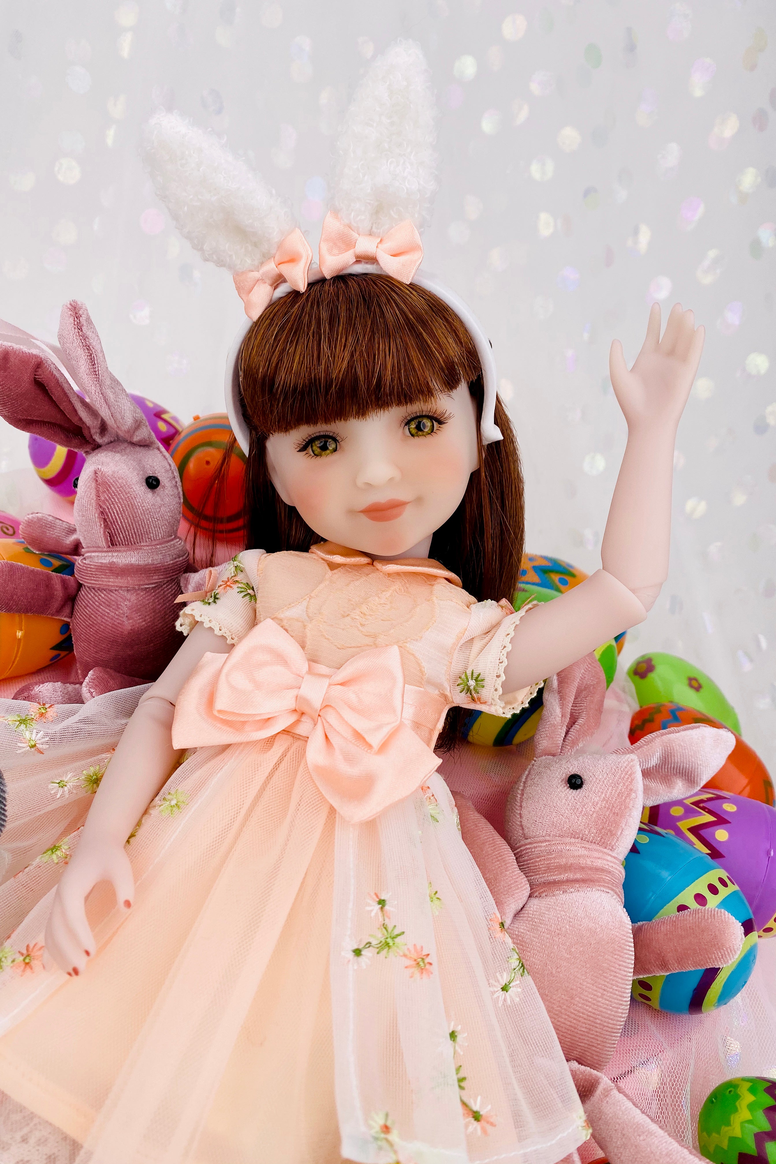 Doll in a peach dress with bunny ears surrounded by Easter-themed plush toys on a light background