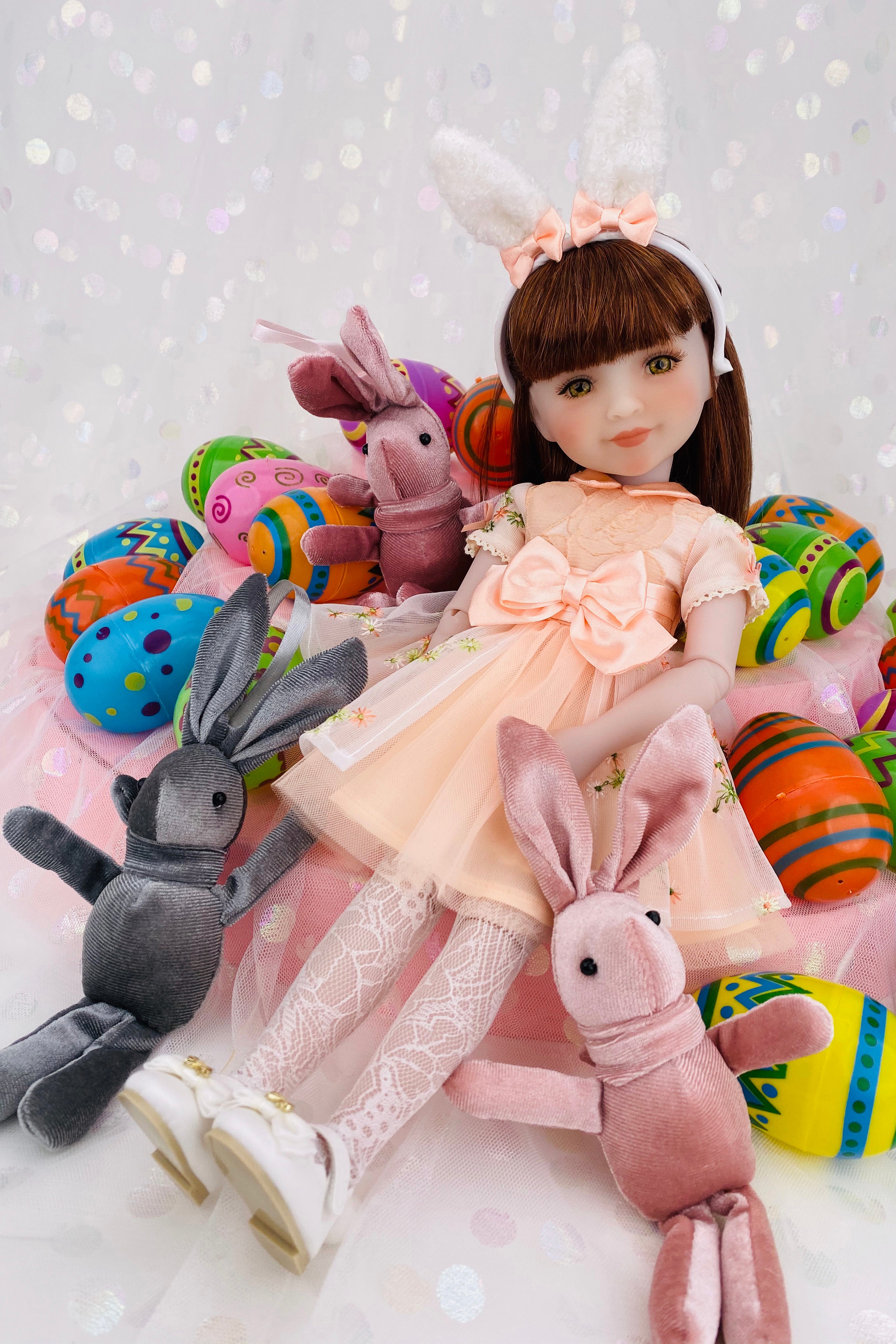 Doll with bunny ears surrounded by plush toys and Easter eggs on a white background