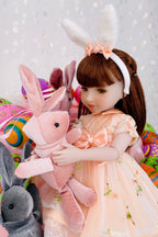 Doll with bunny ears and a pink plush rabbit surrounded by Easter-themed items on a light gray background.