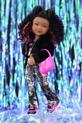 Doll wearing a black jacket, patterned pants, and pink shoes against a colorful, blurred background.