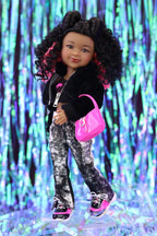 Doll wearing a black jacket, patterned pants, and pink shoes against a colorful, blurred background.