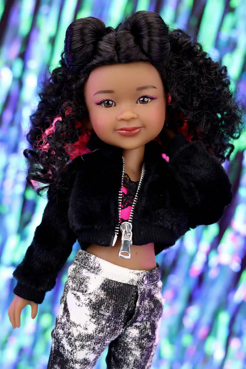 Doll with curly hair wearing a black jacket and patterned pants against a colorful background