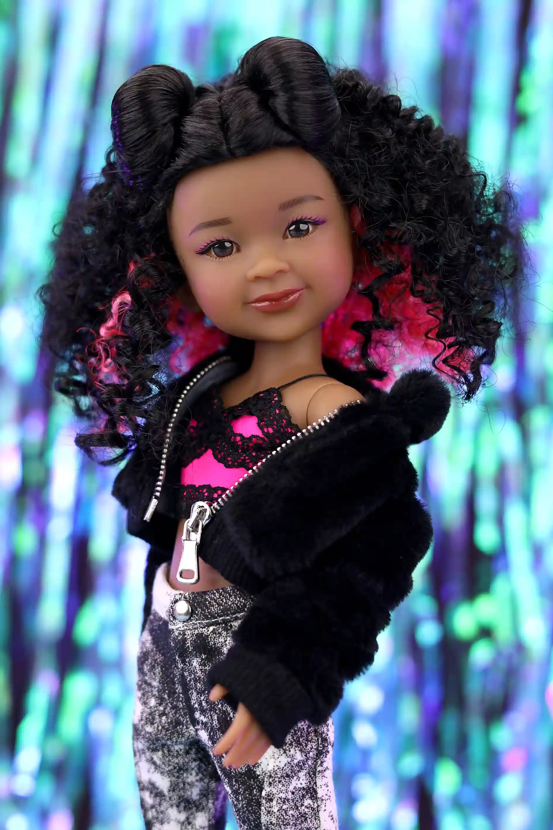 Doll with curly hair wearing a black jacket over a pink top against a colorful, blurred background