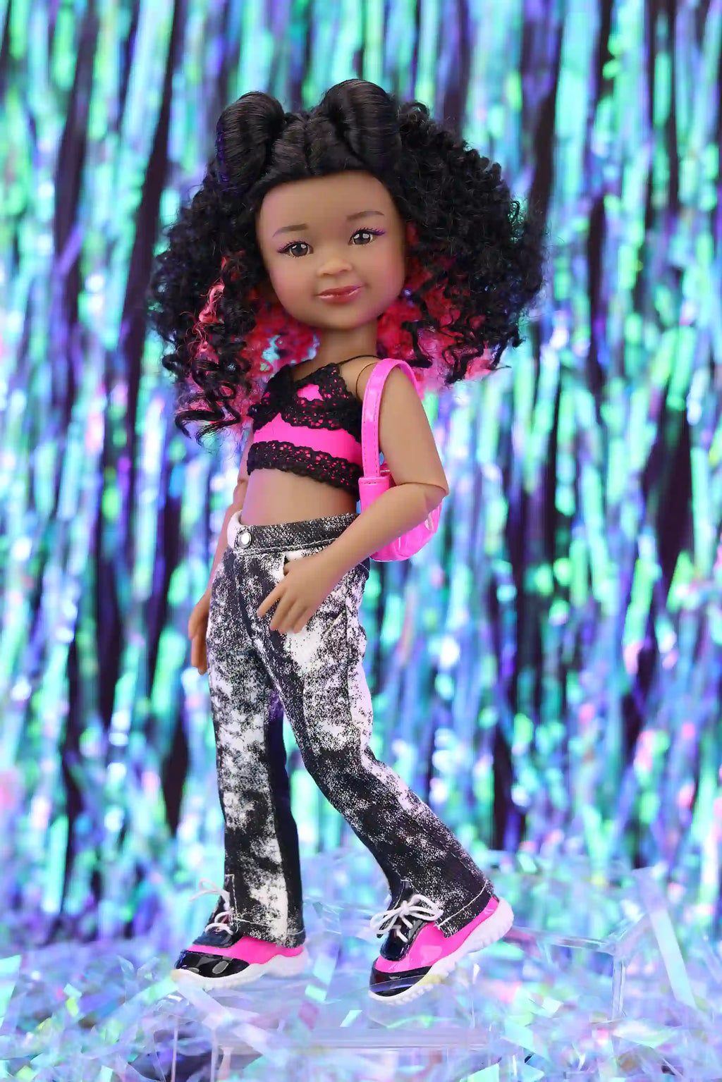 Doll with curly hair wearing a black and pink outfit against a colorful, glittery background
