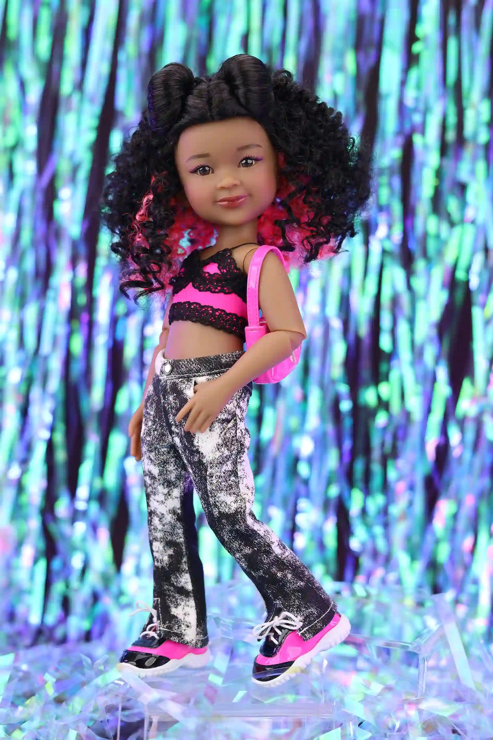 Doll with curly hair wearing a black and pink outfit against a colorful, glittery background