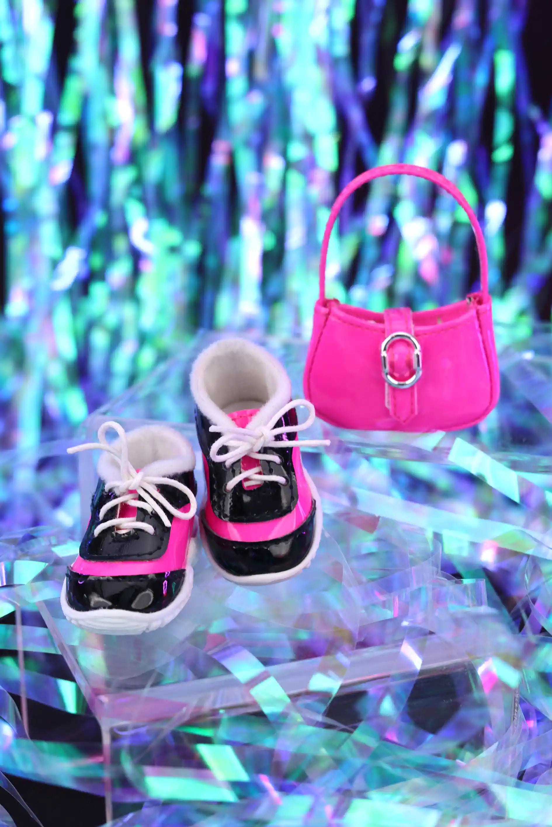 Pair of black and pink shoes with a matching handbag on a reflective surface with colorful, blurred background.