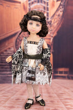 Doll wearing a black and white patterned dress with a decorative headband in an indoor setting.